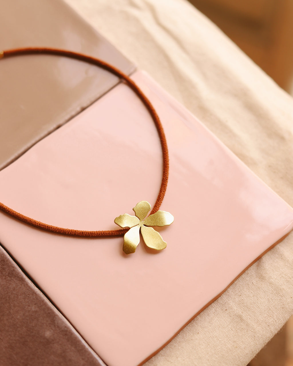 Gargantilha em fio de camurça com pendente dourado em forma de flor